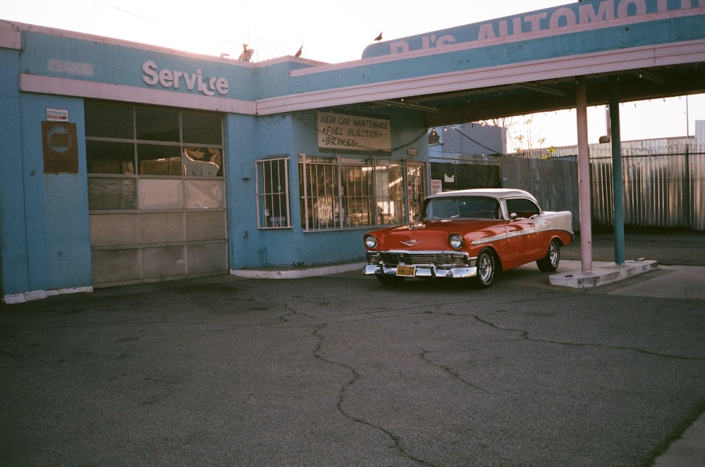 red and white vintage car parked beside blue and white building during daytime