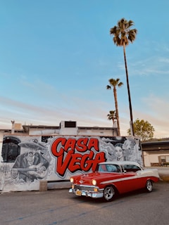 Red Hot Ed standing proudly beside his 1979 red Corvette outside a cozy roadside taco stand with colorful murals.
