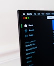 A computer screen displays the Spotify application, showing menu options such as Home, Browse, Radio, and Your Library, which includes Made For You, Recently Played, and Liked Songs. The application interface is sleek, with a dark background and white text, alongside green, yellow, and red window control buttons at the top left.
