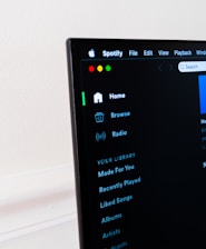 A computer screen displays the Spotify application, showing menu options such as Home, Browse, Radio, and Your Library, which includes Made For You, Recently Played, and Liked Songs. The application interface is sleek, with a dark background and white text, alongside green, yellow, and red window control buttons at the top left.