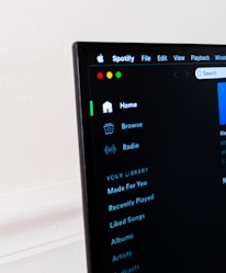 A computer screen displays the Spotify application, showing menu options such as Home, Browse, Radio, and Your Library, which includes Made For You, Recently Played, and Liked Songs. The application interface is sleek, with a dark background and white text, alongside green, yellow, and red window control buttons at the top left.