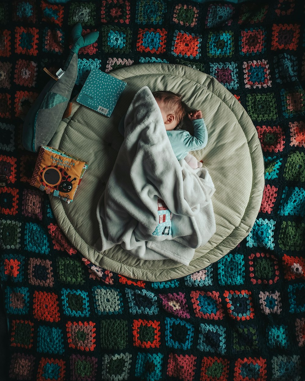 Baby in Weiß Onesie liegt auf weißem und grünem Felsen und spielt Schläfer