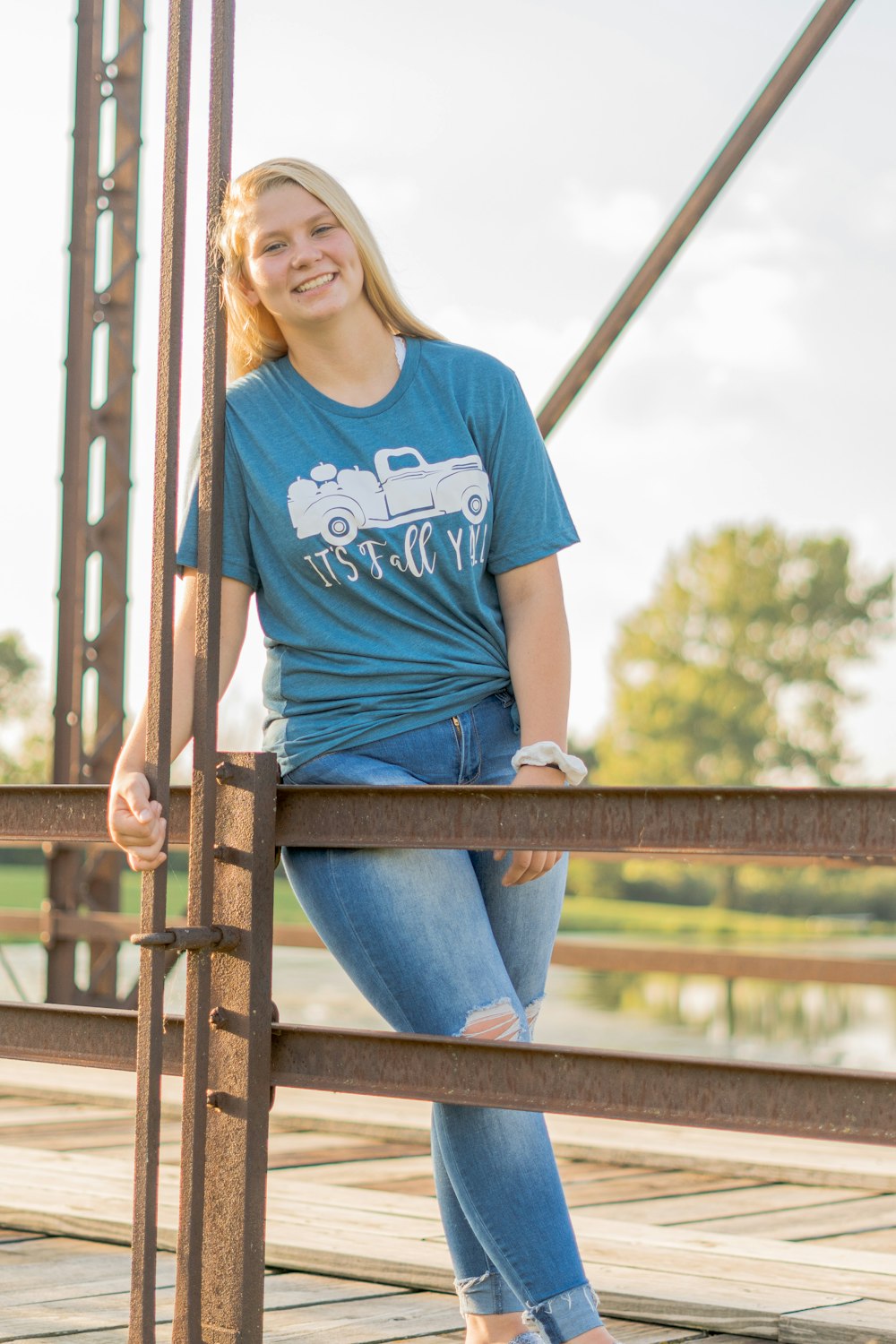 woman in blue crew neck t-shirt and blue denim jeans leaning on brown wooden railings