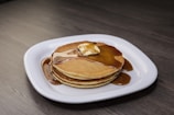 A stack of golden mini pancakes drizzled with maple syrup and a pat of melting butter.