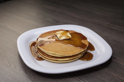 Golden gluten-free pancakes stacked high with maple syrup dripping down the sides.