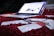 A slightly blurred laptop is open and resting on a red carpet. In the foreground, several credit cards and receipts are scattered across the carpet, suggesting a scene involving online shopping or financial transactions.
