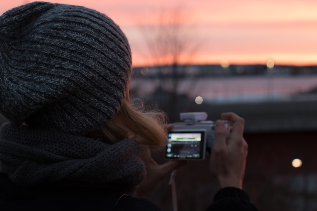 woman in black knit cap holding black and silver camera during sunset