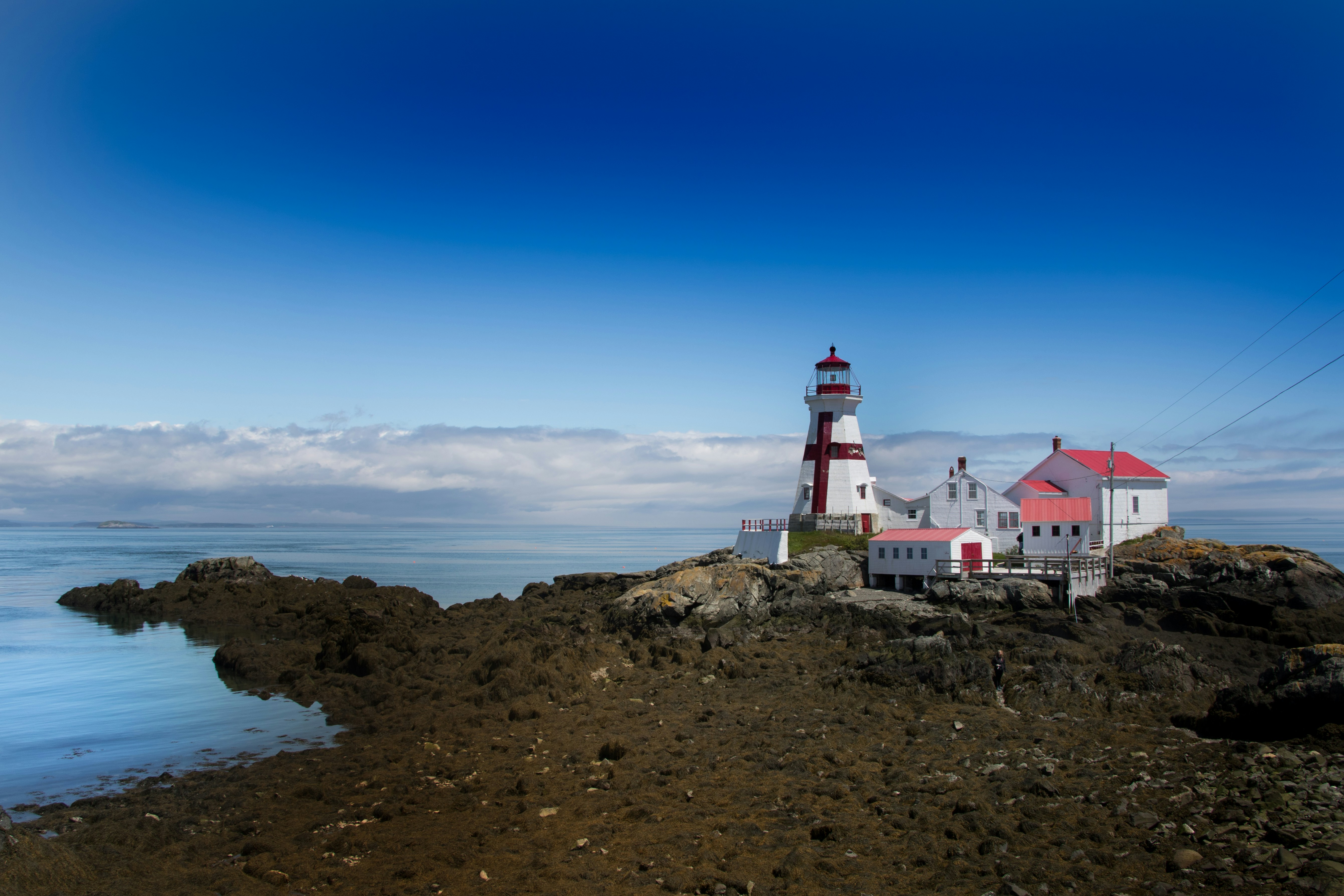 white and red lighthouse on brown rocky hill under blue sky during daytime