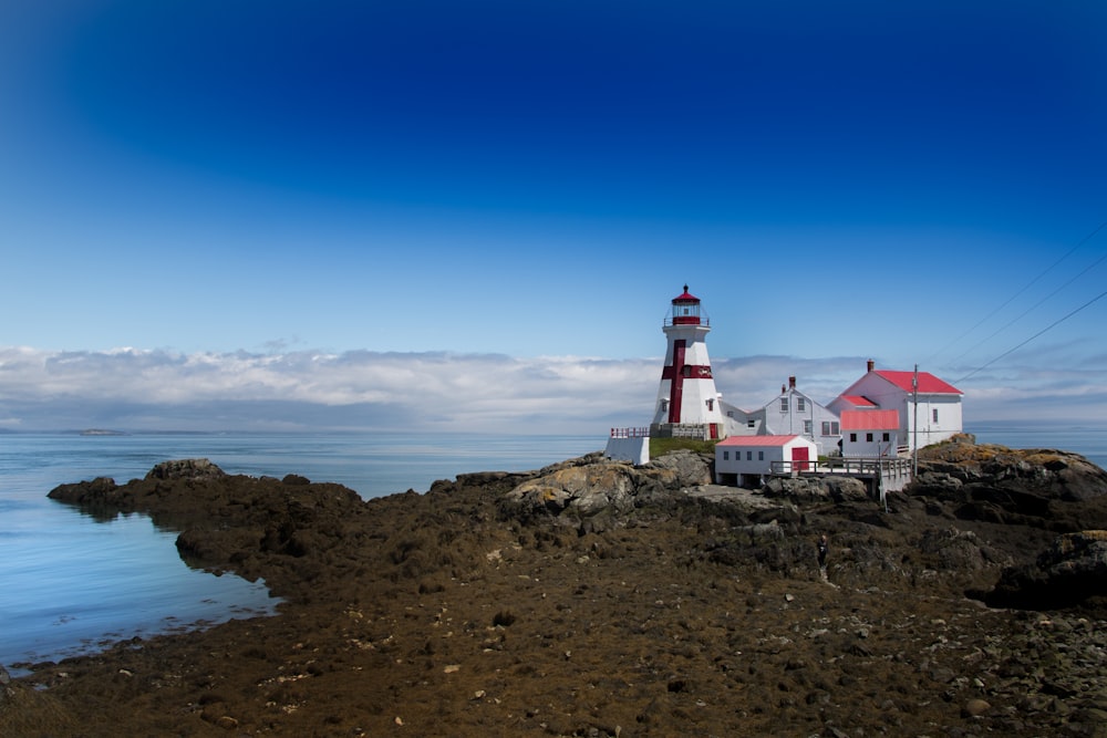 Weißer und roter Leuchtturm auf einem braunen felsigen Hügel unter blauem Himmel tagsüber