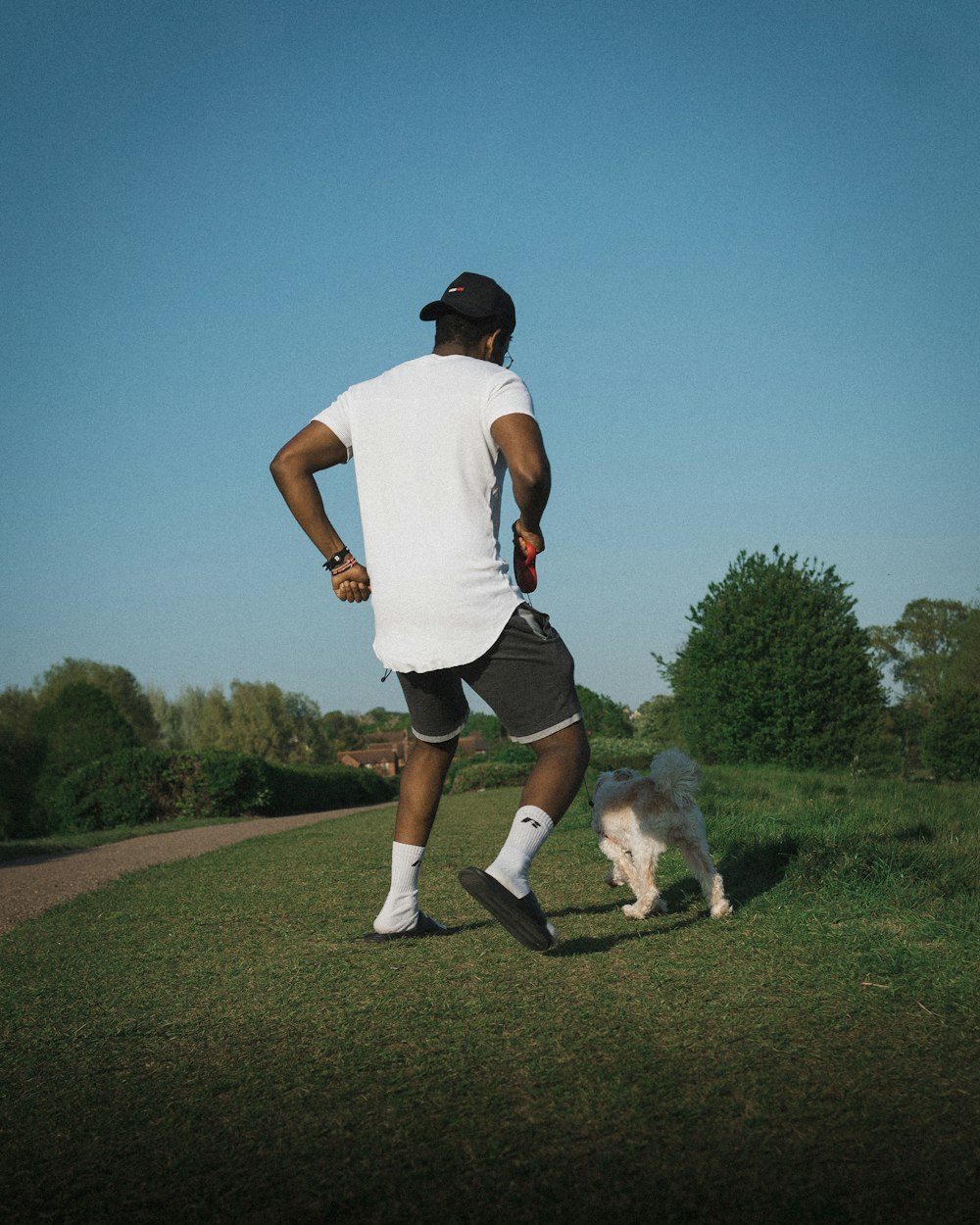 man in white t-shirt and black shorts running on green grass field during daytime
