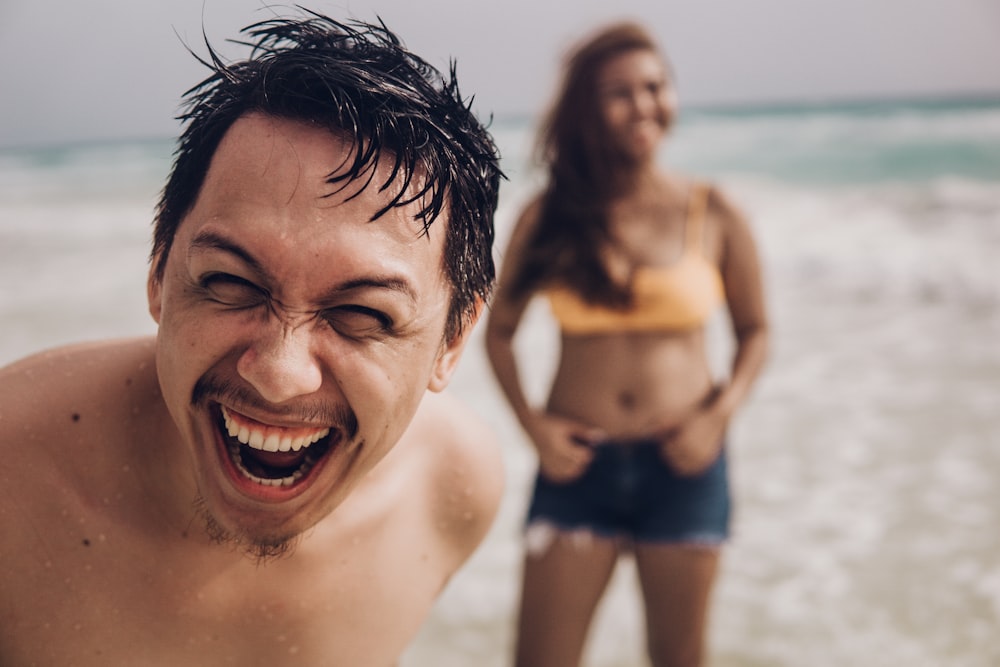 homem sorridente em shorts azuis na praia durante o dia