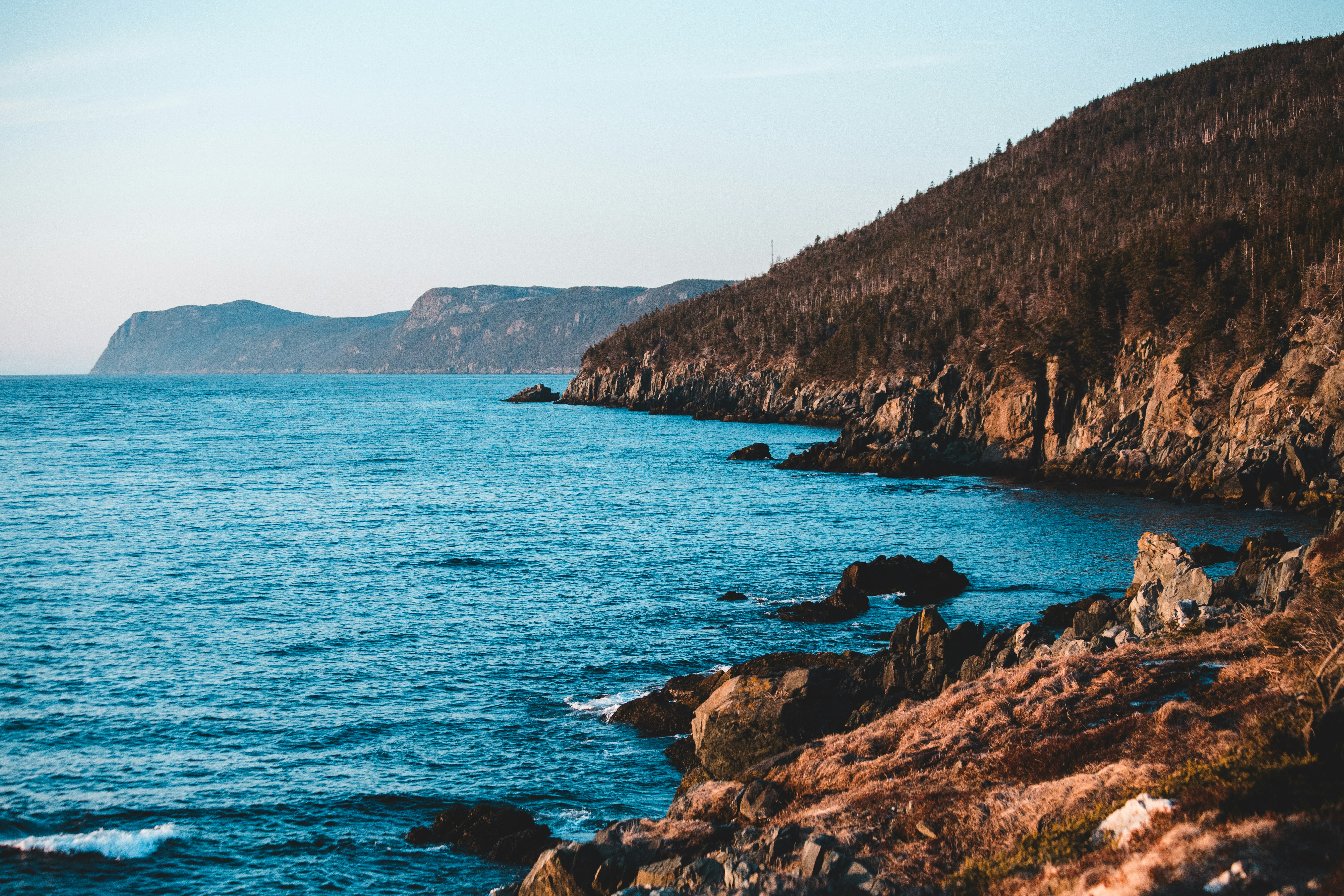 brown rocky mountain beside blue sea under blue sky during daytime