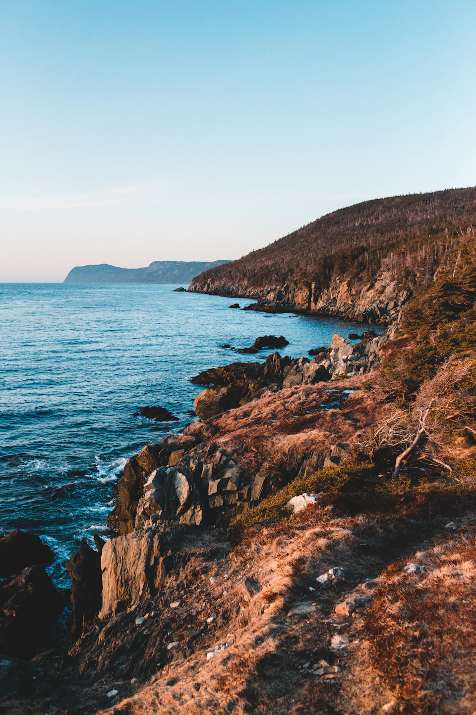 Serene coastal landscape with rocky cliff face reflecting clear blue sky above water