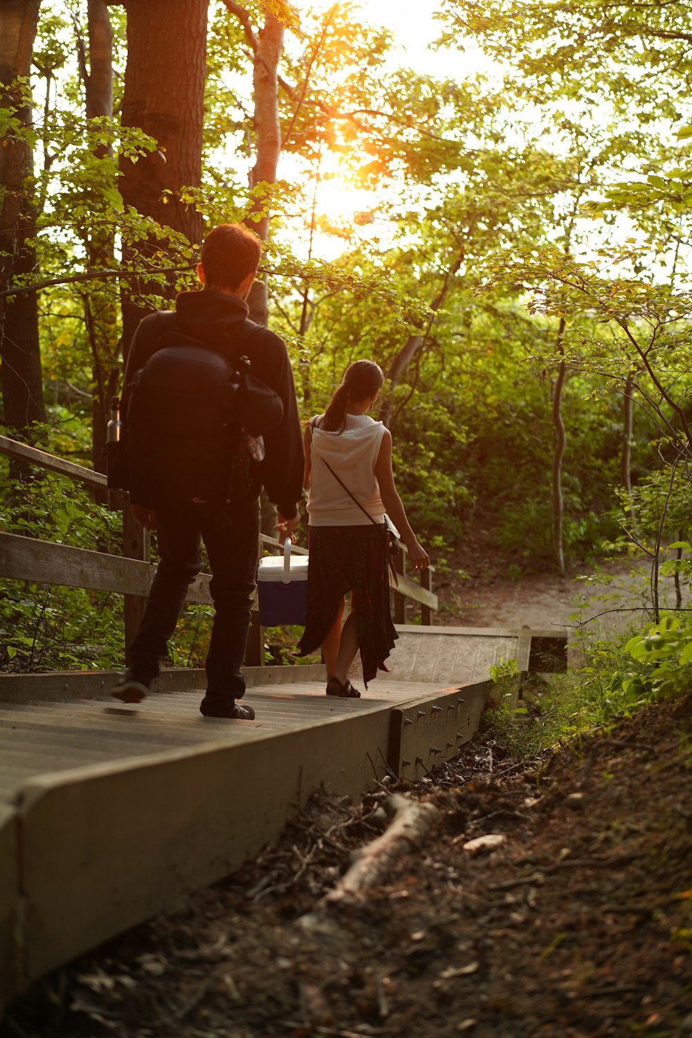 uomo e donna che camminano sul sentiero tra gli alberi durante il giorno