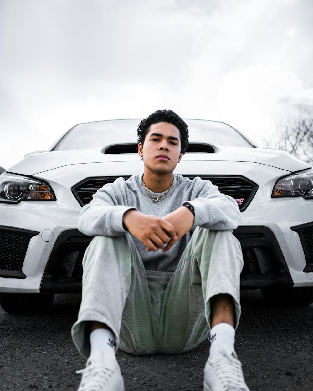 man in gray long sleeve shirt and green pants sitting on gray car hood during daytime