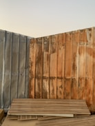 Corrugated metal sheets with visible rust and weathering form a corner and are stacked with wooden planks leaning against them. The sky is clear in the background.
