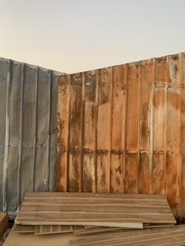 Corrugated metal sheets with visible rust and weathering form a corner and are stacked with wooden planks leaning against them. The sky is clear in the background.