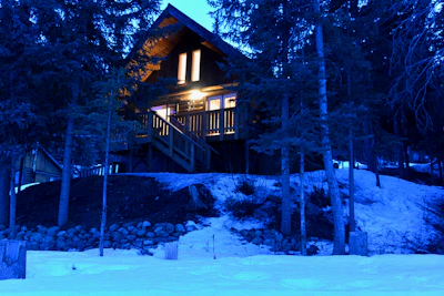 A cozy cabin nestled in snowy woods, glowing warmly against the winter twilight.
