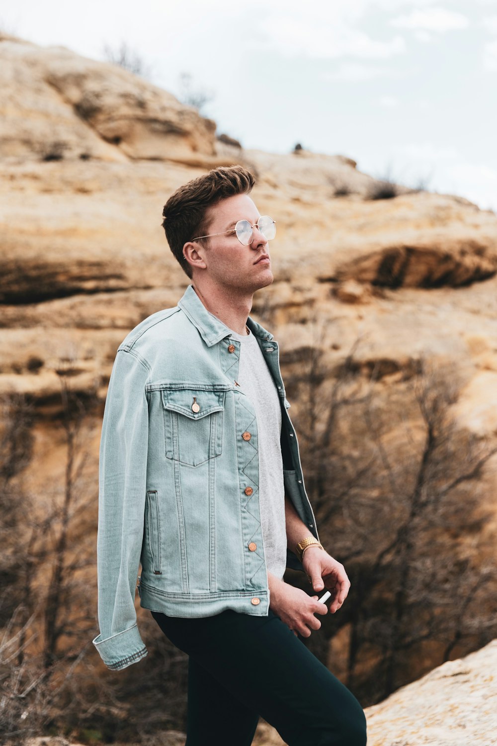 man in blue denim button up jacket standing near brown rock formation during daytime