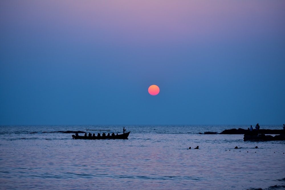 silhouette of people riding boat on sea during sunset