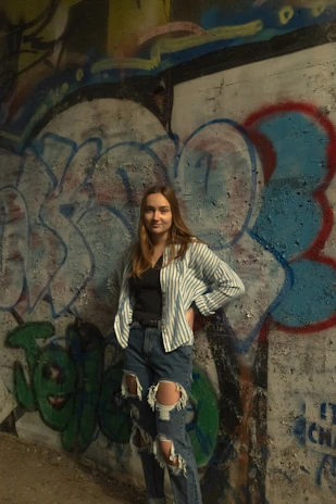 A young woman wearing a cozy oversized sweater paired with trendy high-waisted jeans, standing against a graffiti wall.