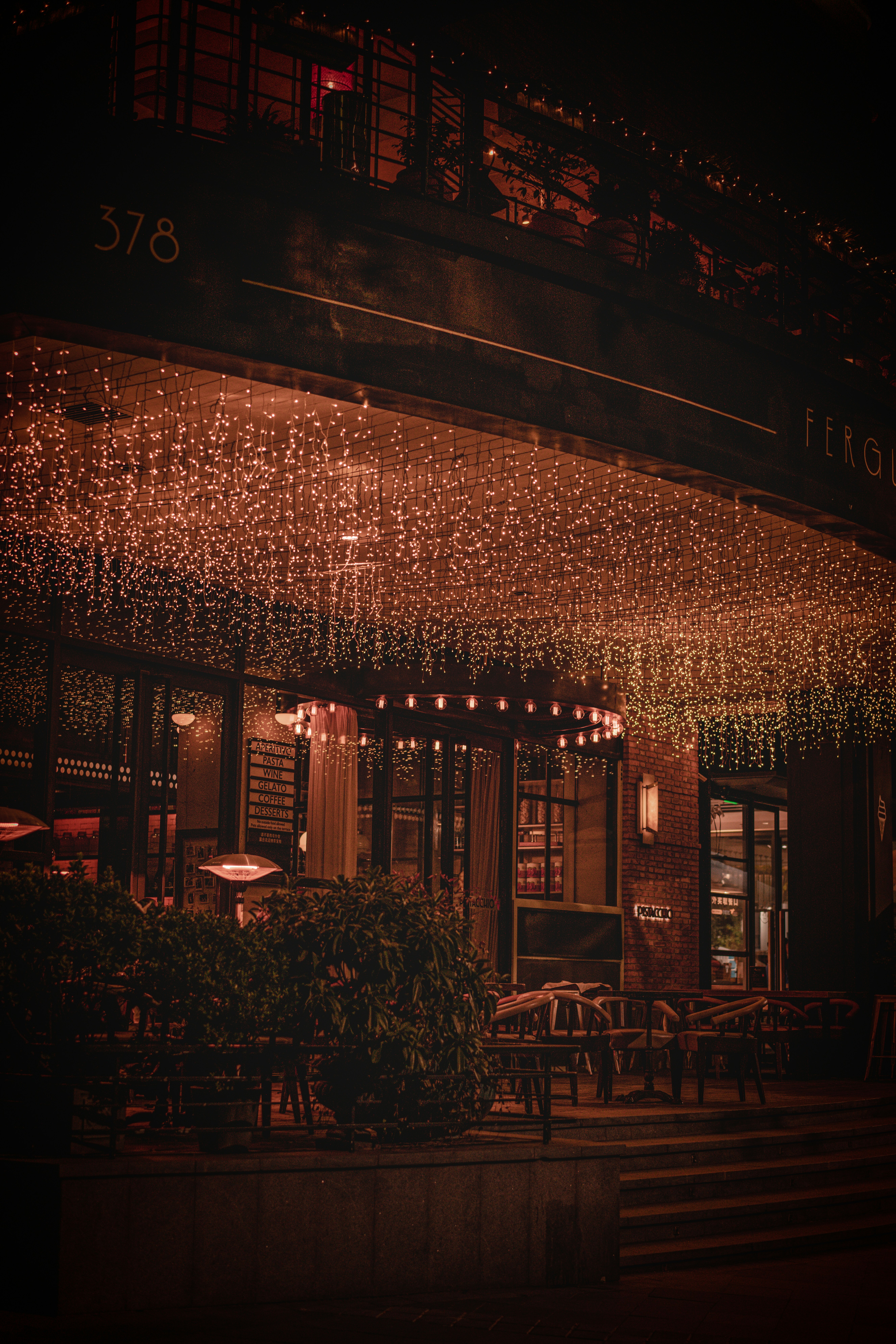 Dimly lit al fresco restaurant with string lights and wooden tables at night, warm amber atmosphere