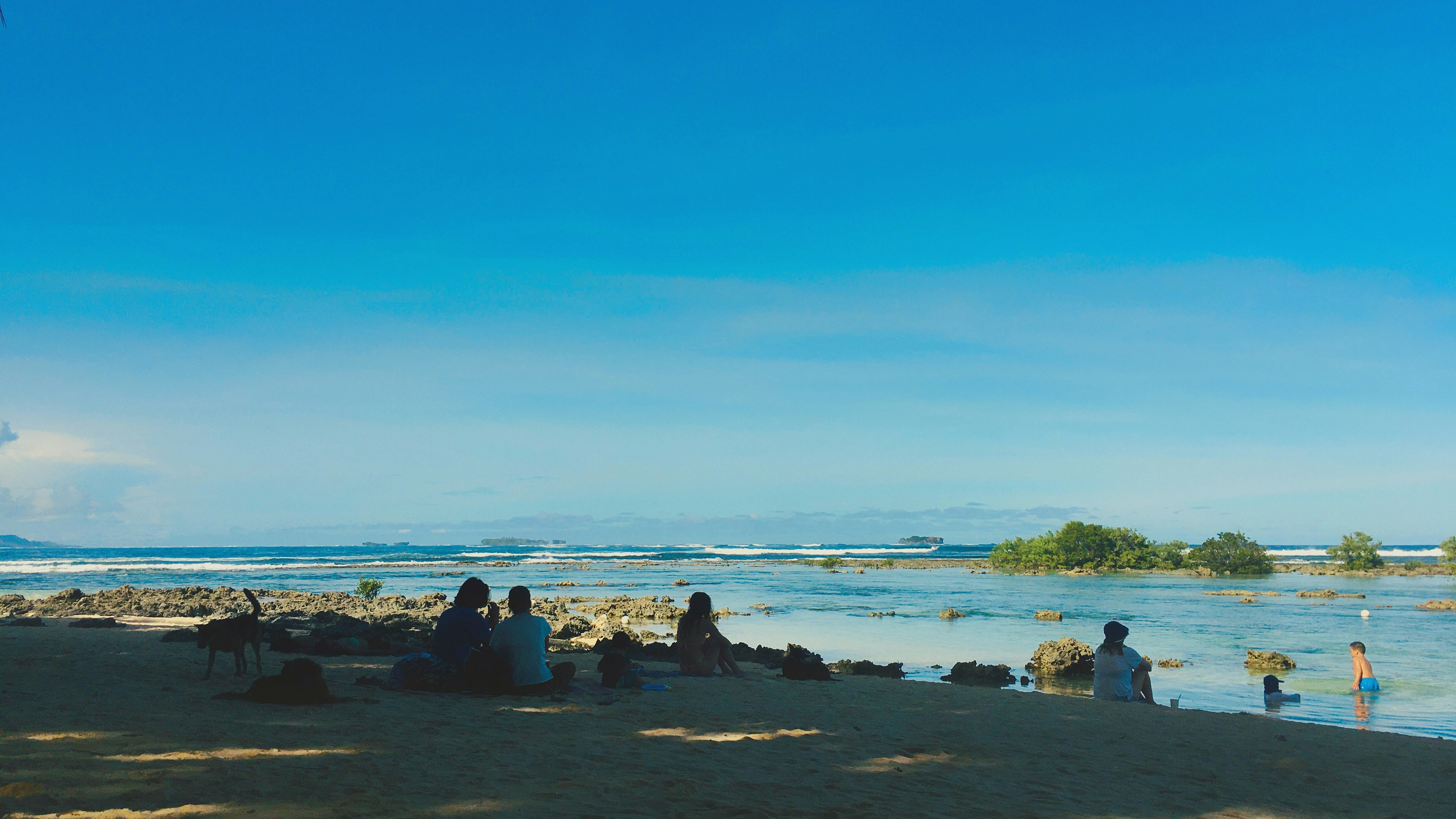people sitting on rock formation near sea during daytime