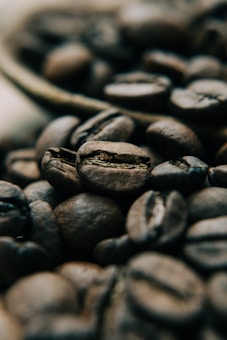 A close-up view of several coffee beans, displaying their rich, brown texture and detailed grooves. The image focuses on the natural patterns and highlights on the beans, creating a warm and inviting atmosphere.