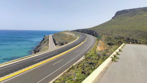 Wide open coastal road with rolling green hills under a bright blue sky, a convertible cruising down the tarmac