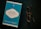 A blue book titled 'Go Kiss the World' by Subroto Bagchi is placed next to a pair of round eyeglasses on a dark surface. The book cover features a white and black circular design with text and a small penguin logo at the top.