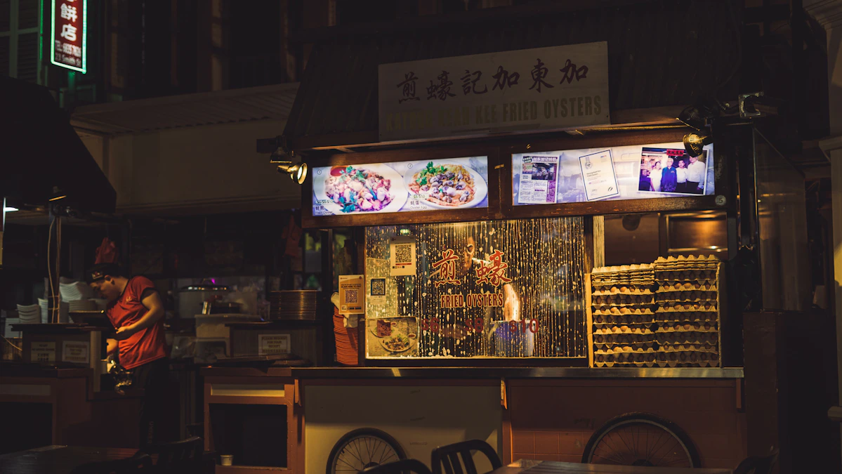 A Kuala Lumpur street food stall stacked with cooked dishes under warm lights.