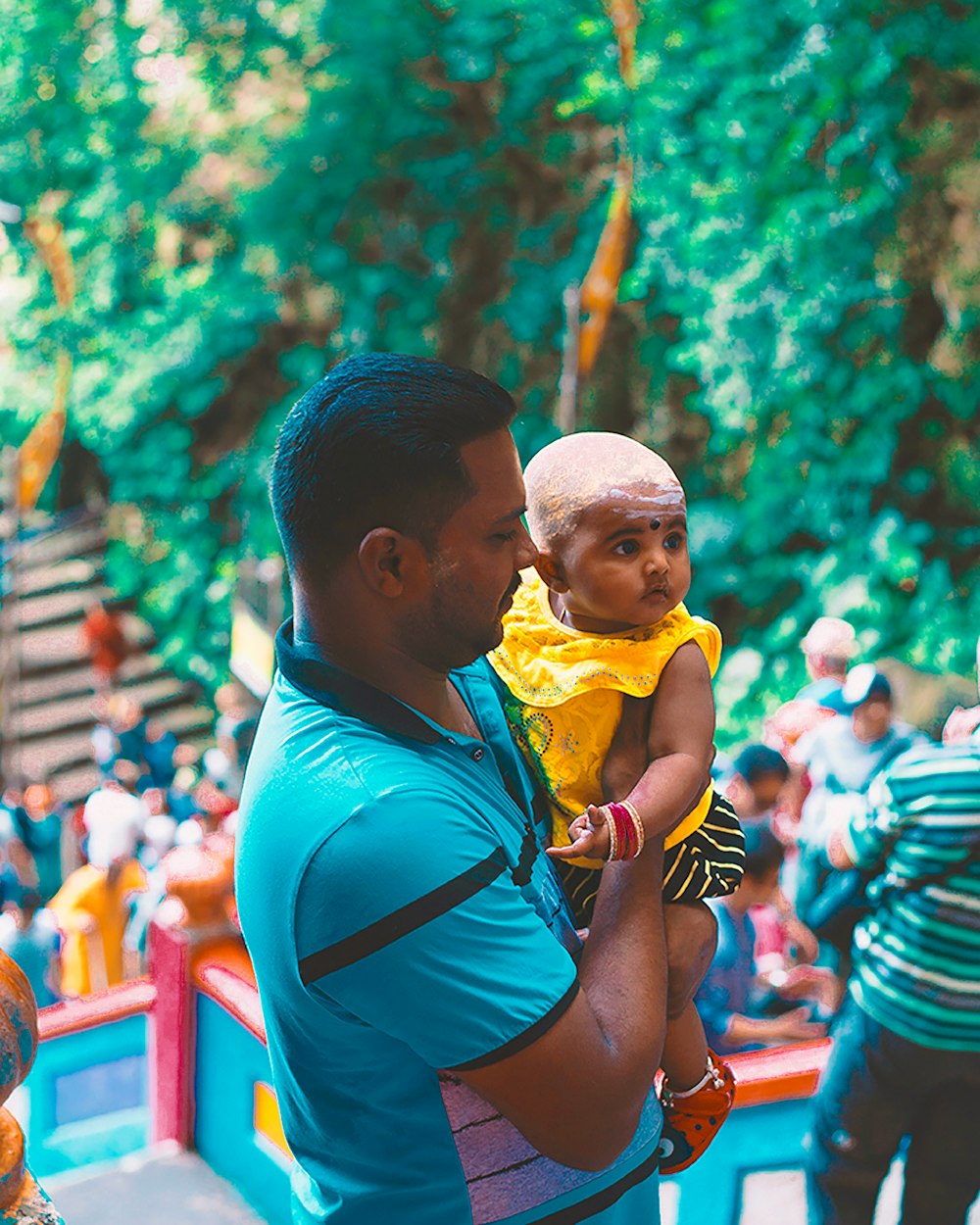 Mann im blauen Tanktop trägt Baby im gelben Hemd