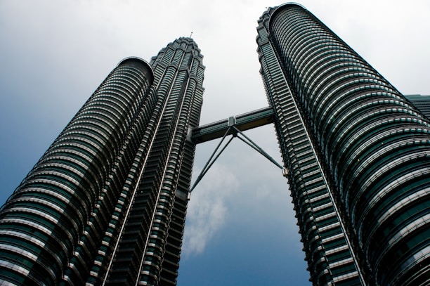 Two towering skyscrapers are connected by a sky bridge near the top, giving a sense of grandeur and modern architectural design. The buildings feature a series of concentric rings, creating a futuristic texture as they rise towards the sky.