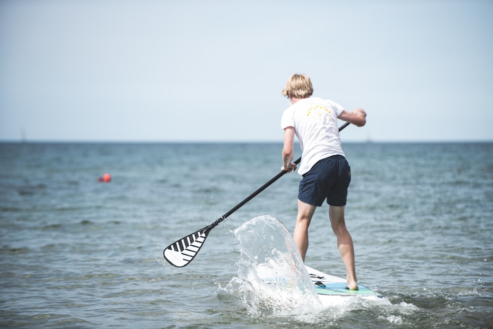 girl in white shirt and black shorts standing on white surfboard during daytime