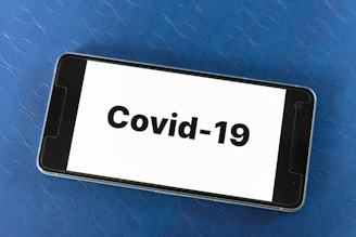 A smartphone placed on a blue textured surface displaying the text 'Covid-19' prominently on its screen.