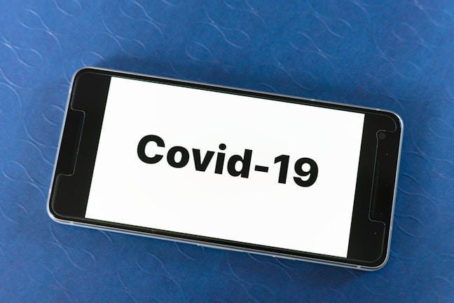 A smartphone placed on a blue textured surface displaying the text 'Covid-19' prominently on its screen.