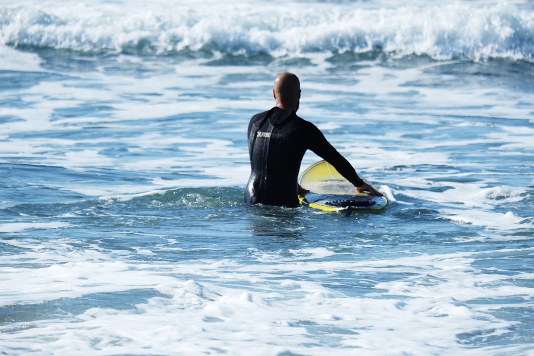 man in black wet suit holding yellow surfboard on sea during daytime