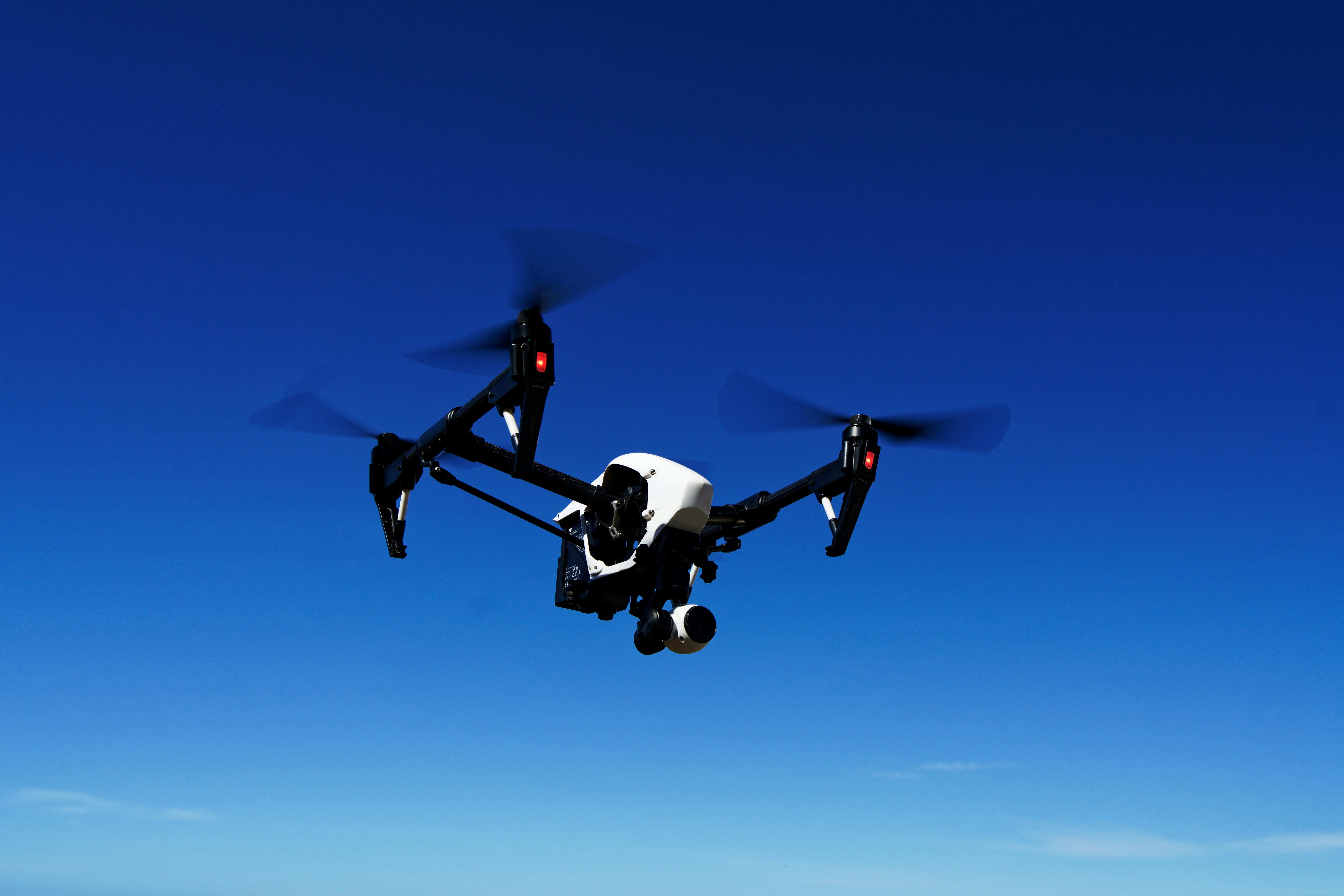 The high performance DJI Inspire 1.2 UAV flying in a blue sky with the landing gear up in flying position. 