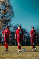 3 men in red jersey shirt standing on green grass field during daytime