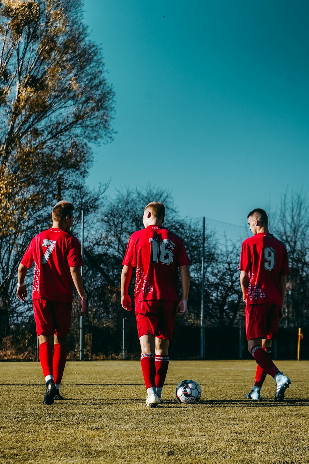 3 men in red jersey shirt standing on green grass field during daytime