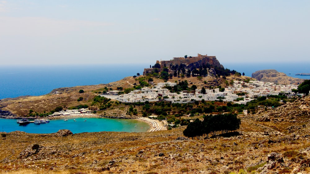 brown and green mountain beside blue sea under blue sky during daytime