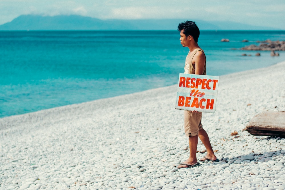 topless man holding white and red happy birthday signage standing on beach during daytime