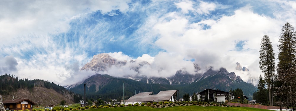 brown wooden house near green trees and mountain under white clouds during daytime