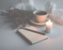 white candle on white ruled paper beside white ceramic mug