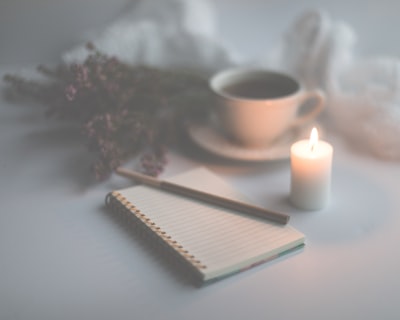 white candle on white ruled paper beside white ceramic mug candle teams background