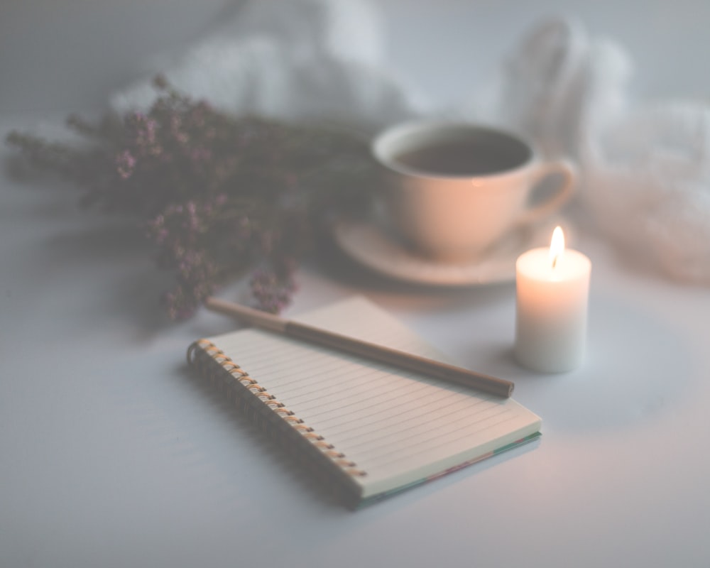 white candle on white ruled paper beside white ceramic mug