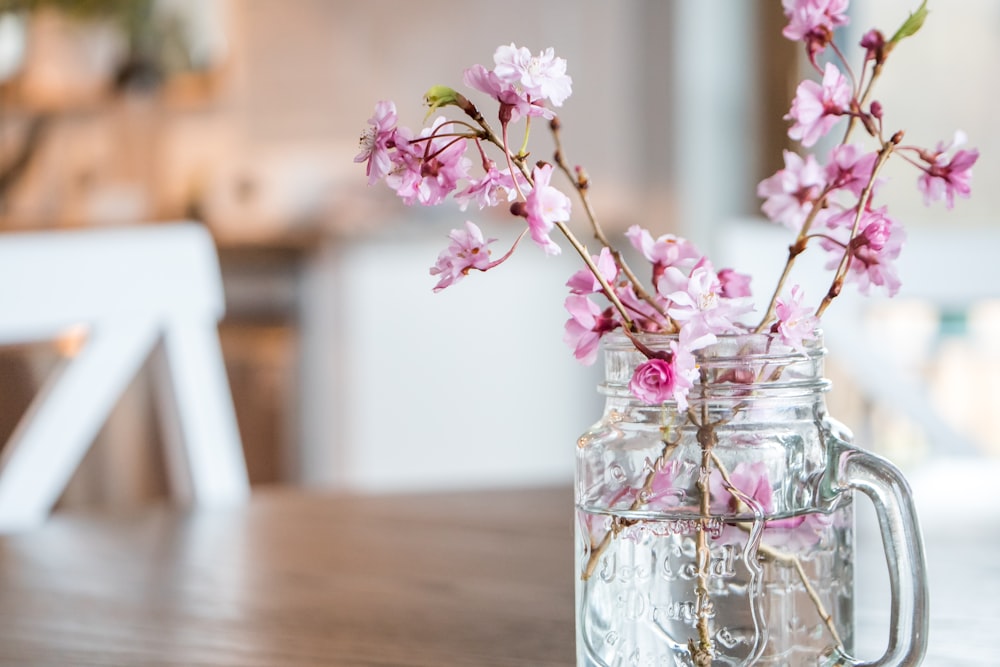 flores rosadas en frasco de vidrio transparente sobre mesa de madera marrón
