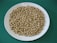 A white plate filled with a large quantity of dry chickpeas rests on a green surface. The chickpeas are uniformly arranged and appear uncooked.