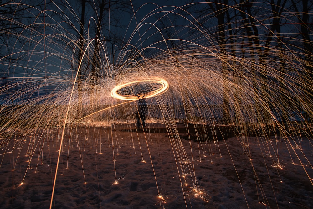 steel wool photography of man in black jacket standing on gray sand