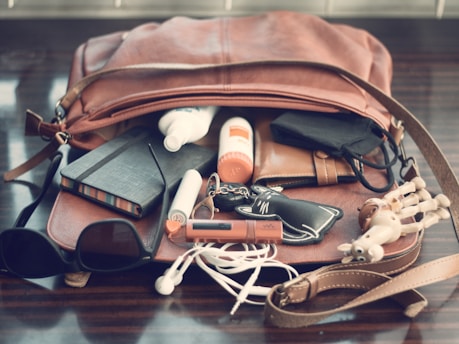 black sunglasses beside white earbuds and brown leather bag